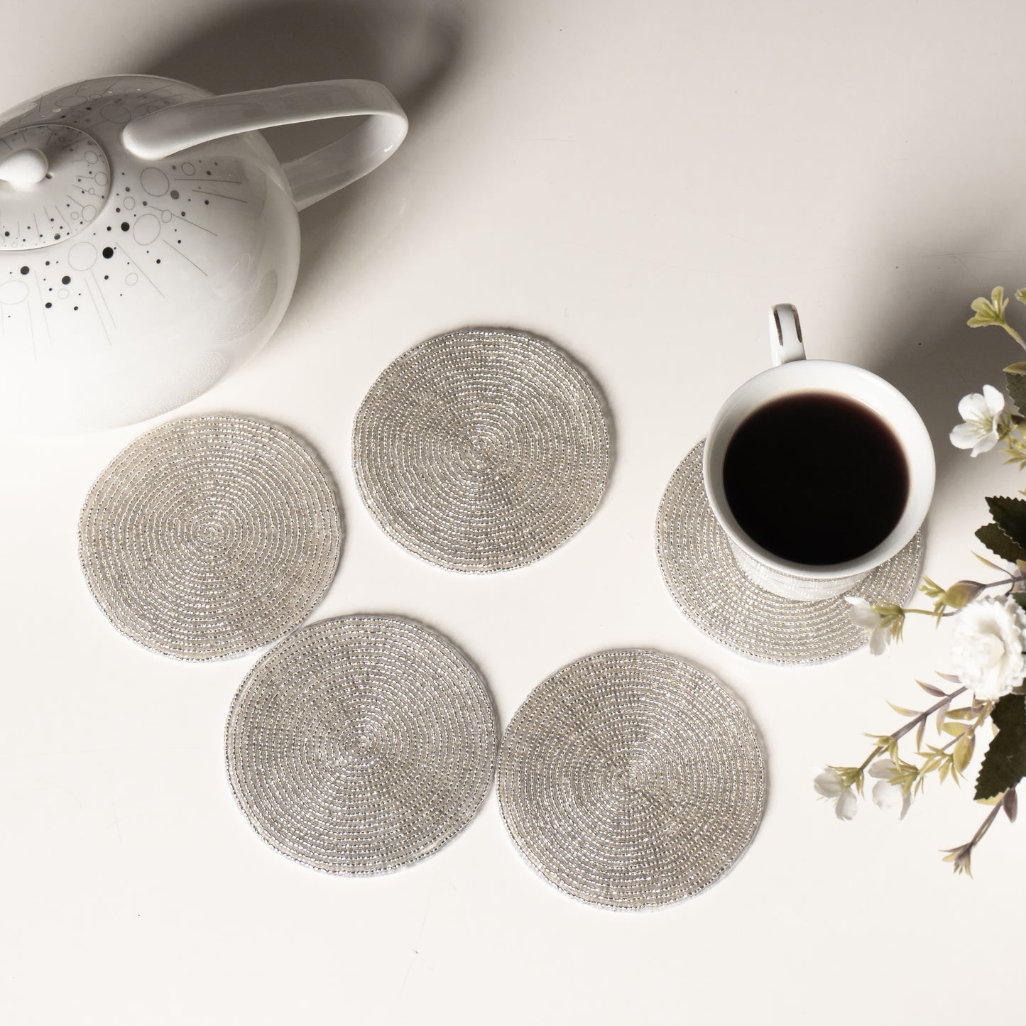 Set of round woven coasters on a table with a teapot and cup.