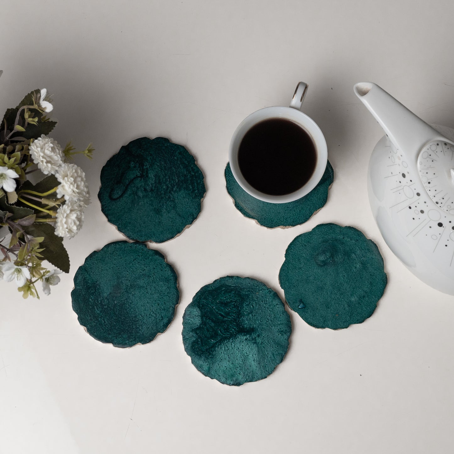 Teal coasters with a cup of coffee and teapot on a light surface.