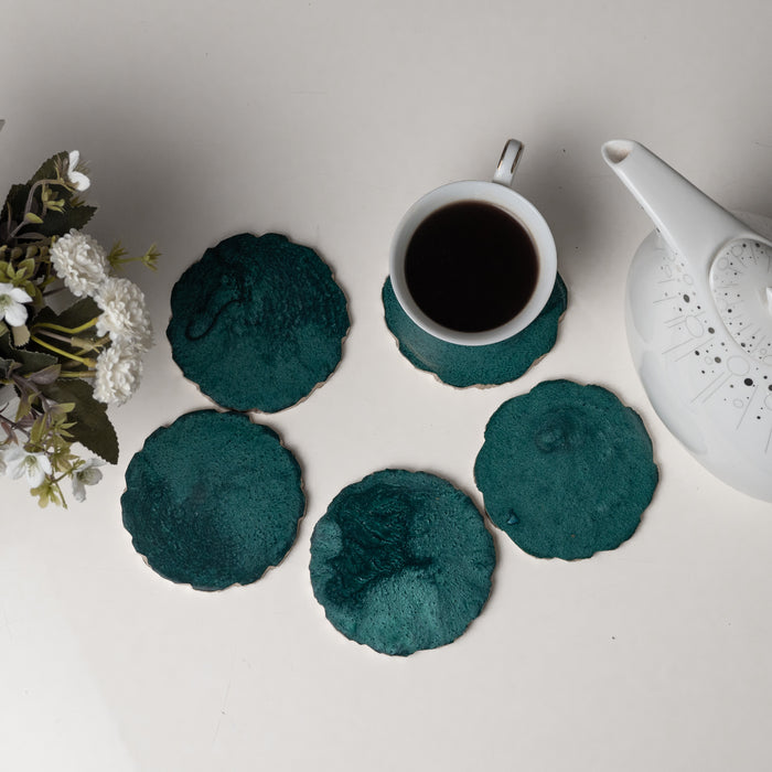 Teal coasters with a cup of coffee and teapot on a light surface.