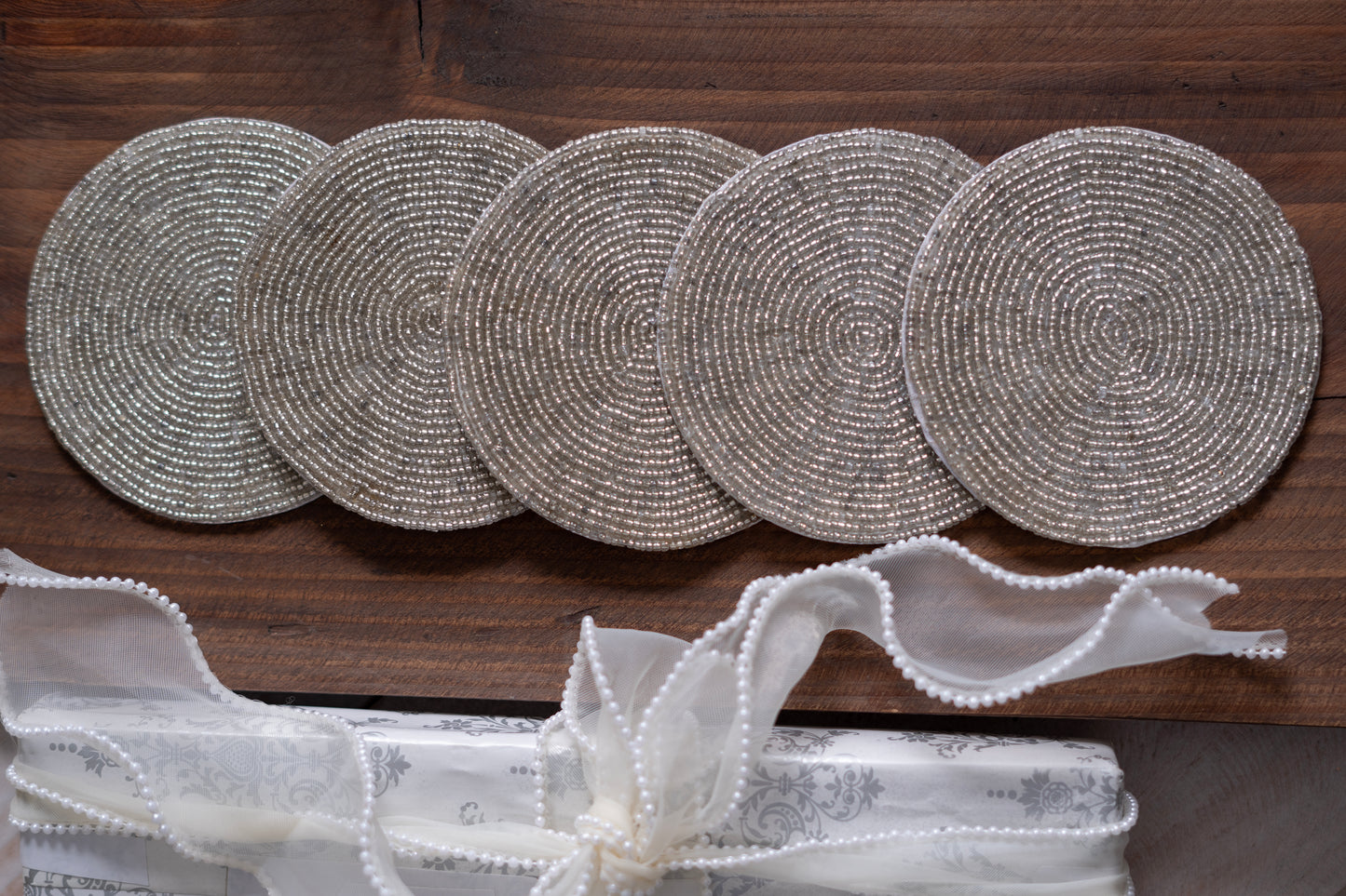 A set of round glass bead coasters with a boho look, displayed on a wooden surface, with a white beaded trim in the foreground.