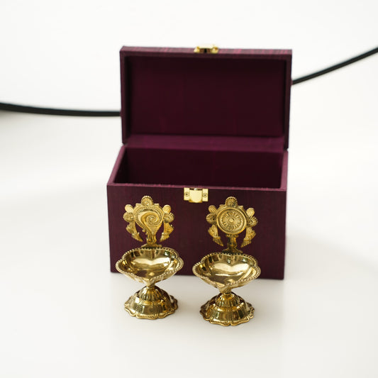 Two gold decorative items on a white surface with a maroon box in the background.