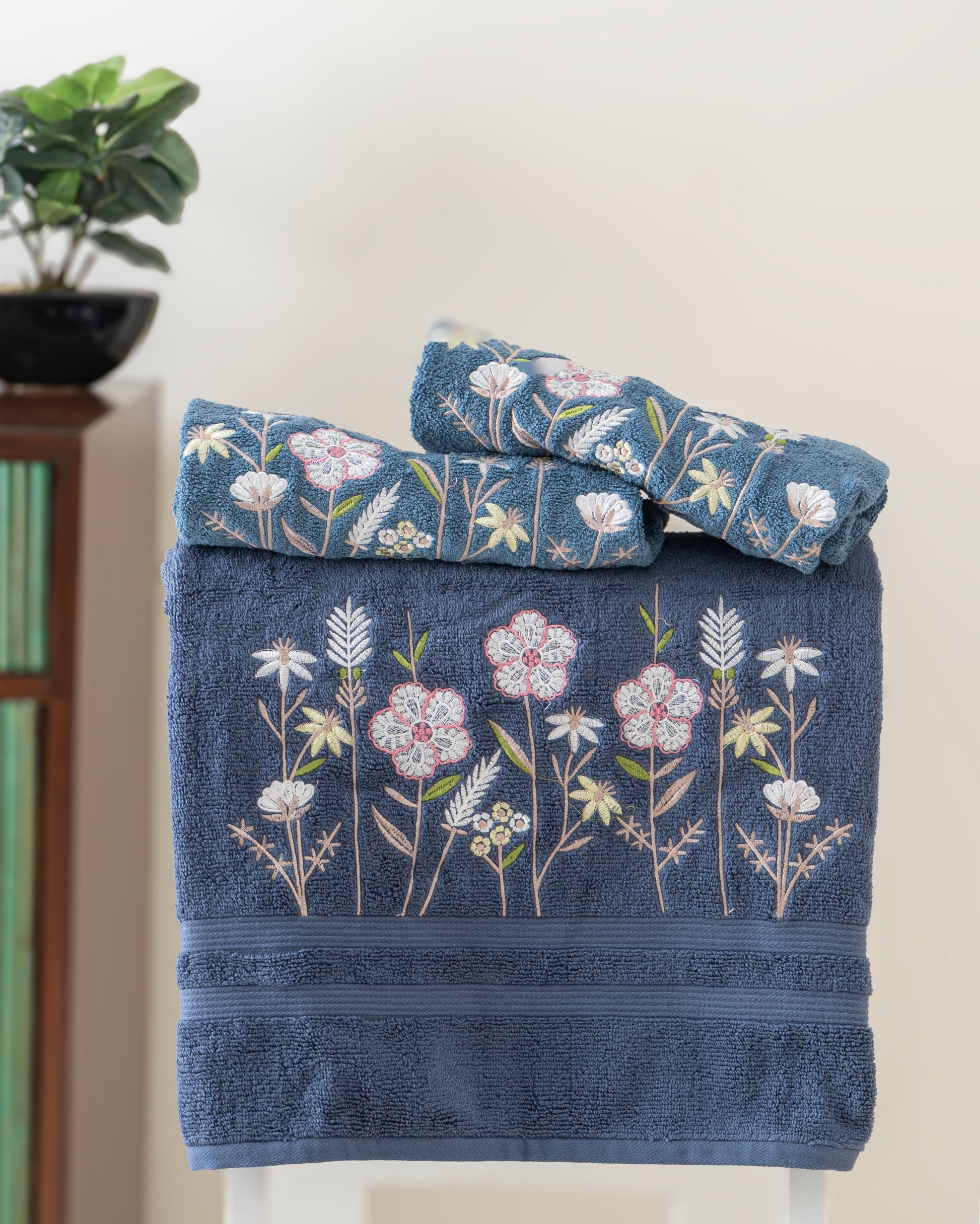 Blue towels with floral embroidery on a white surface, with a plant in the background.