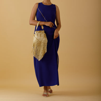 Woman in a blue dress holding a gold handbag against a beige background