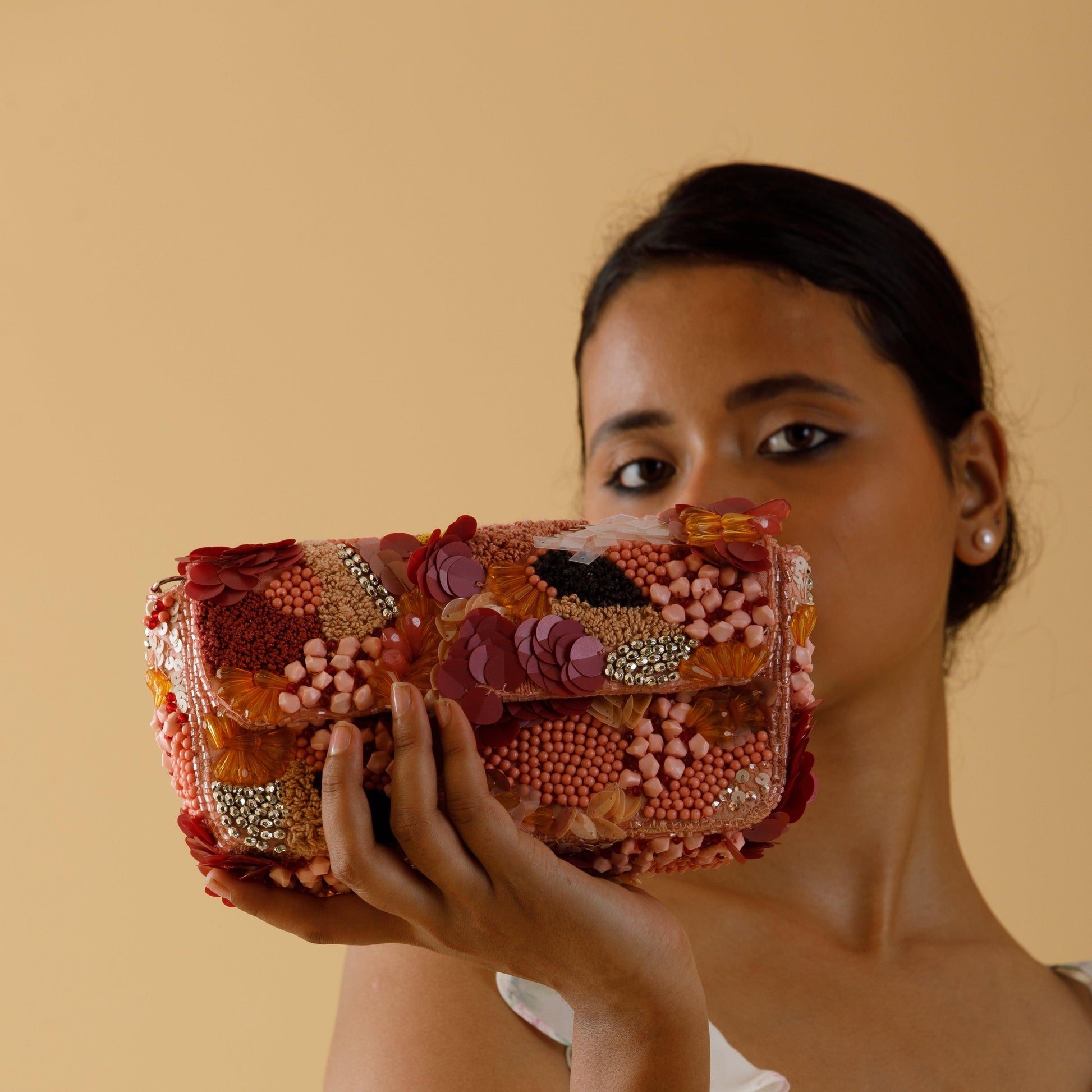Woman holding a colorful, embellished handbag against a beige background