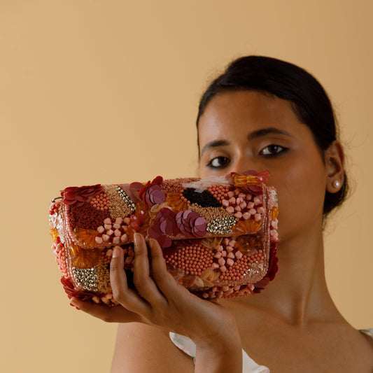 Woman holding a colorful, embellished handbag against a beige background