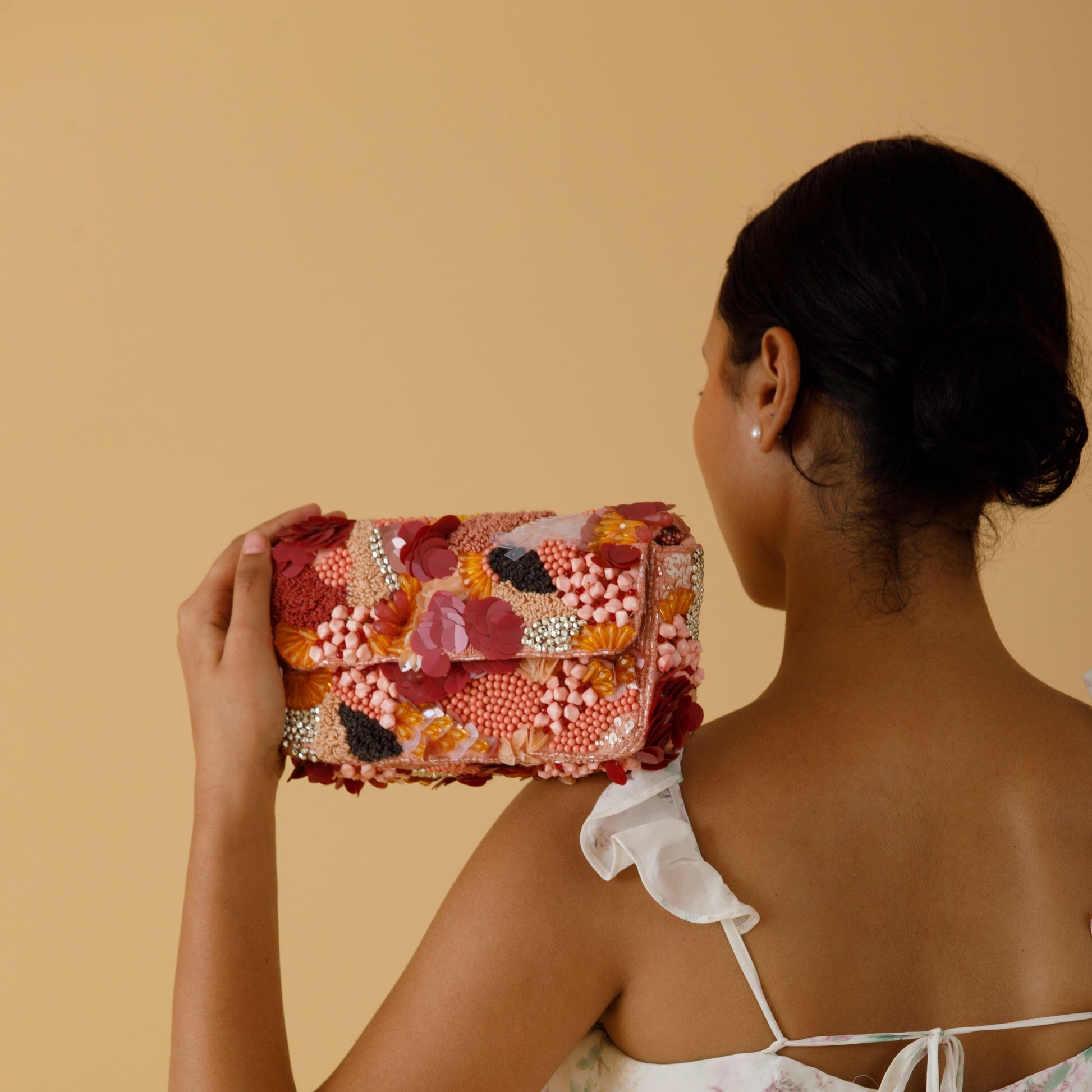 Woman holding a colorful floral clutch against a beige background