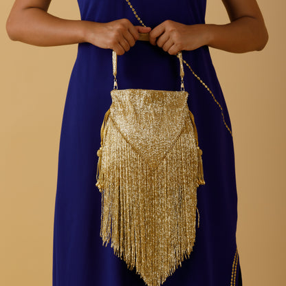 Gold fringe handbag held by a person wearing a blue dress on a beige background