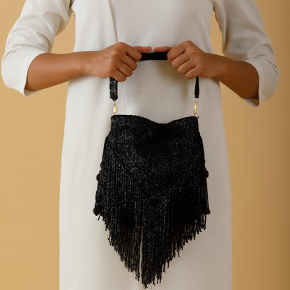 Person holding a black fringed handbag against a beige background