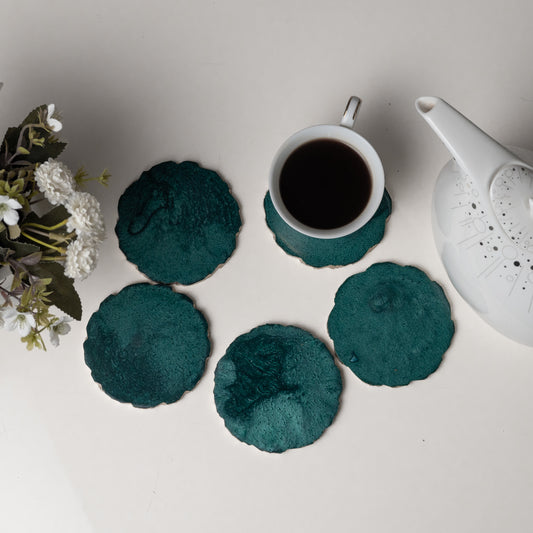 Teal coasters with a cup of coffee and teapot on a light surface.