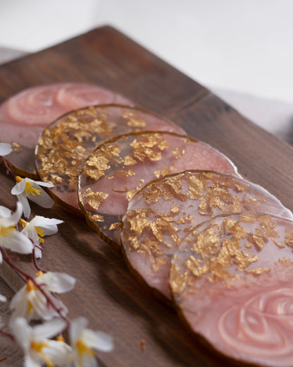 Coasters with gold leaf design on a wooden surface with white flowers.