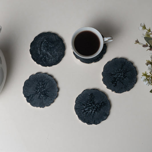 Set of four dark gray coasters with a white mug on a light surface.