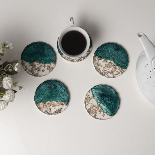 Set of four teal and beige coasters with a cup of coffee and teapot on a light surface.