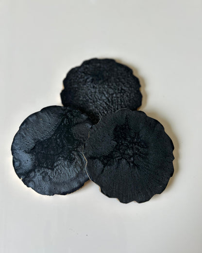 Three black textured coasters on a light gray background