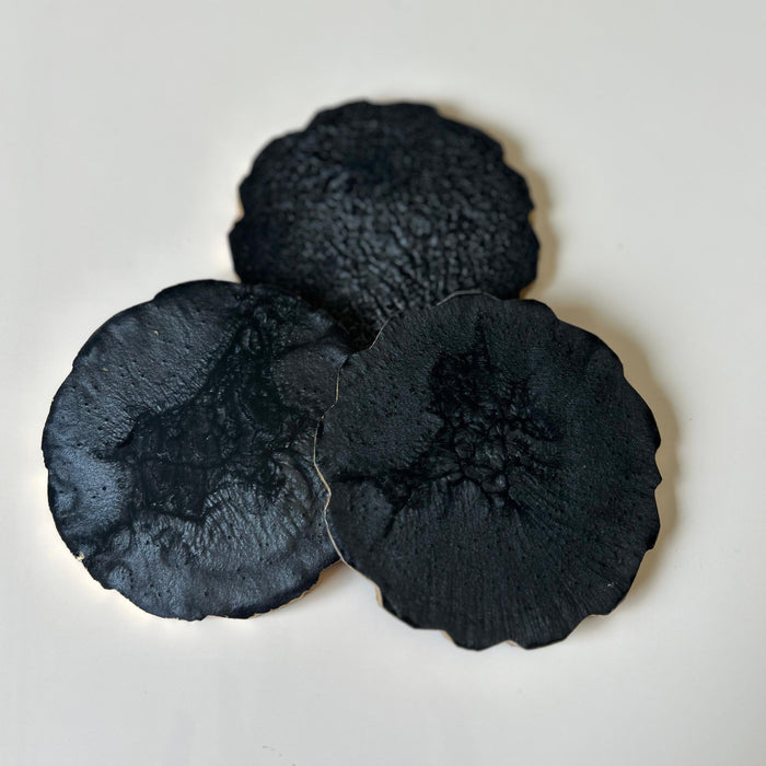 Three black textured coasters on a light gray background